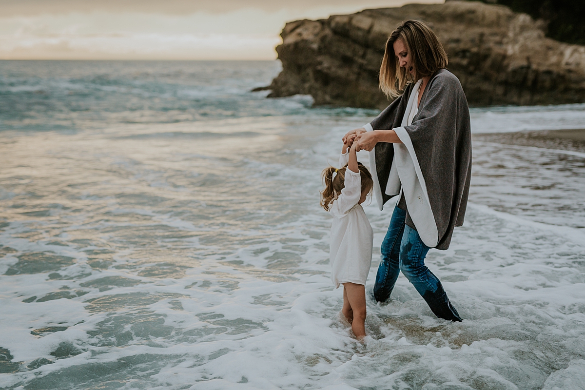 Orange County family photographer. Mom swings daughter around in the ocean waves at Table Rock Beach Laguna Beach during photo session with Krystil McDowall Photography