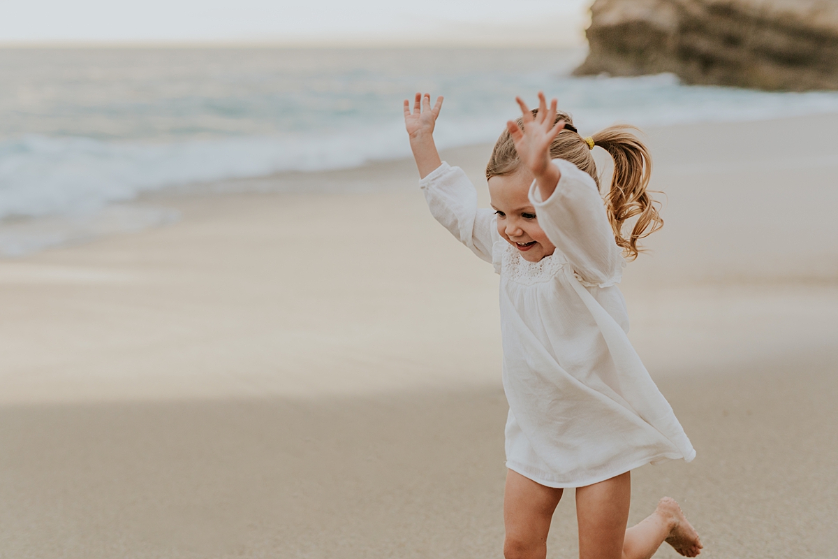 Orange County family photographer. Two year old girl runs across the sand at Table Rock Beach Laguna Beach during photo session with Krystil McDowall Photography