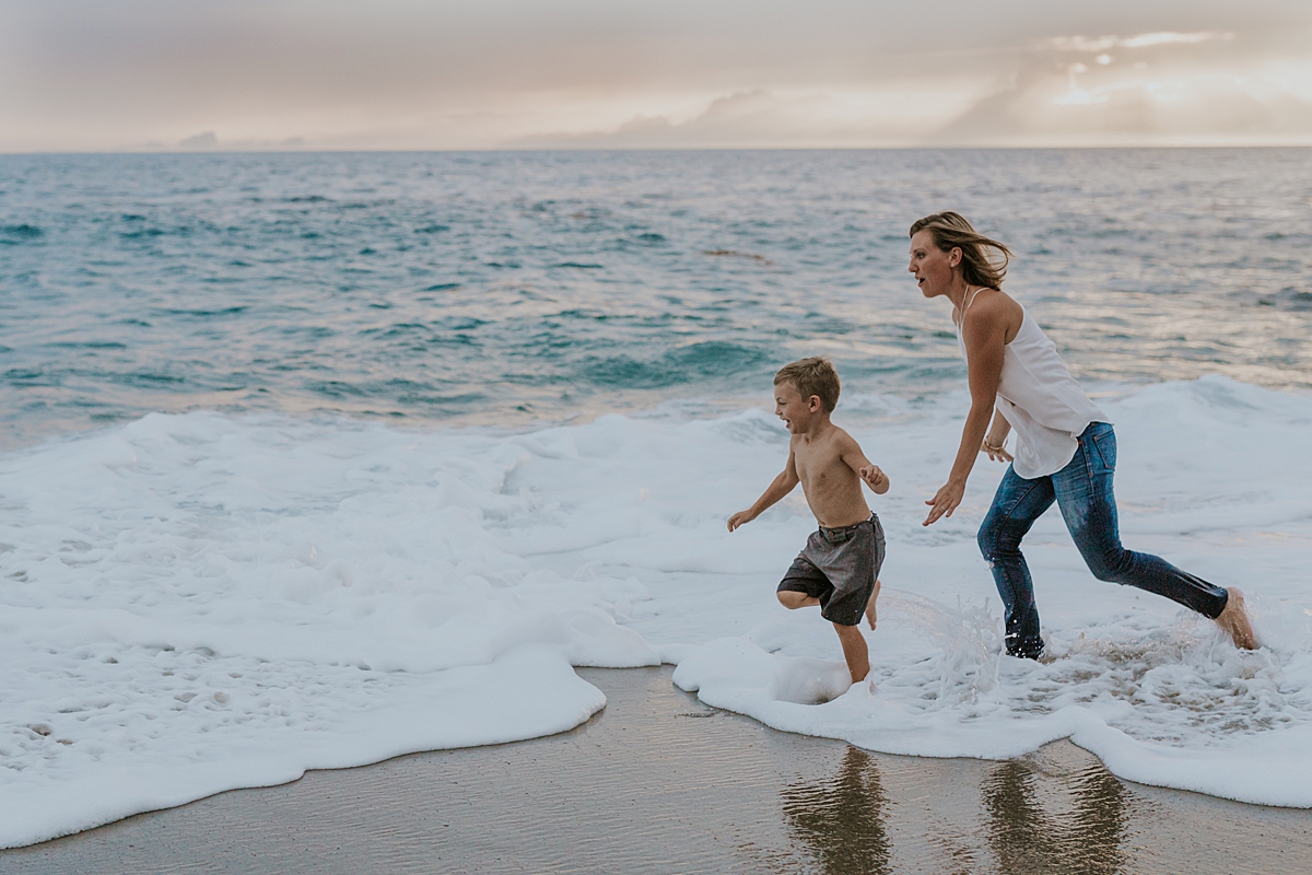 Orange County family photographer. Mom chases her four year old boy in the shallow waves at Table Rock Beach Laguna Beach during photo session with Krystil McDowall Photography