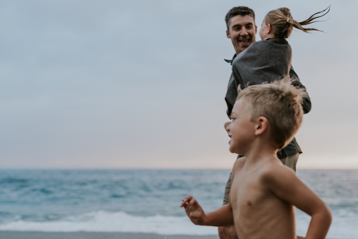 Orange County family photographer. Candid image of dad, daughter and son running along the sand at Table Rock Beach Laguna Beach during photo session with Krystil McDowall Photography