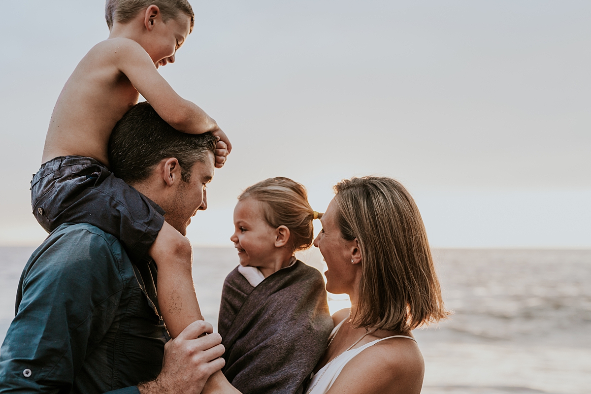 Orange County family photographer. Family of four snuggles in for close time at sunset at Table Rock Beach Laguna Beach during photo session with Krystil McDowall Photography