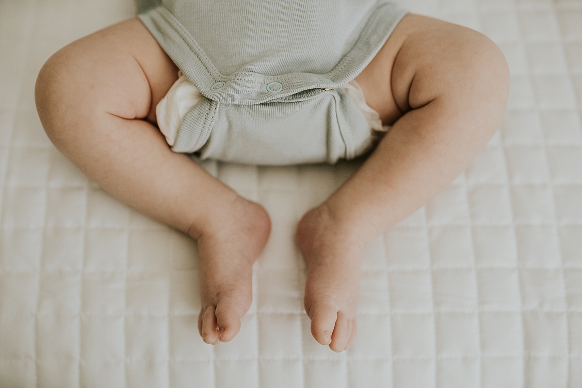 Orange County family photographer. Close up photo of newborn boys legs as he peacefully sleeps on his mom and dad's bed during in-home newborn session with Krystil McDowall Photography