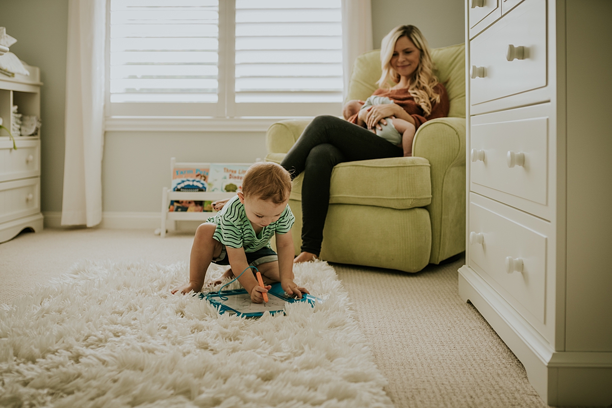 Orange County family photographer. Candid photo of mom rocking her newborn son while her toddler son plays with toys in front of her
