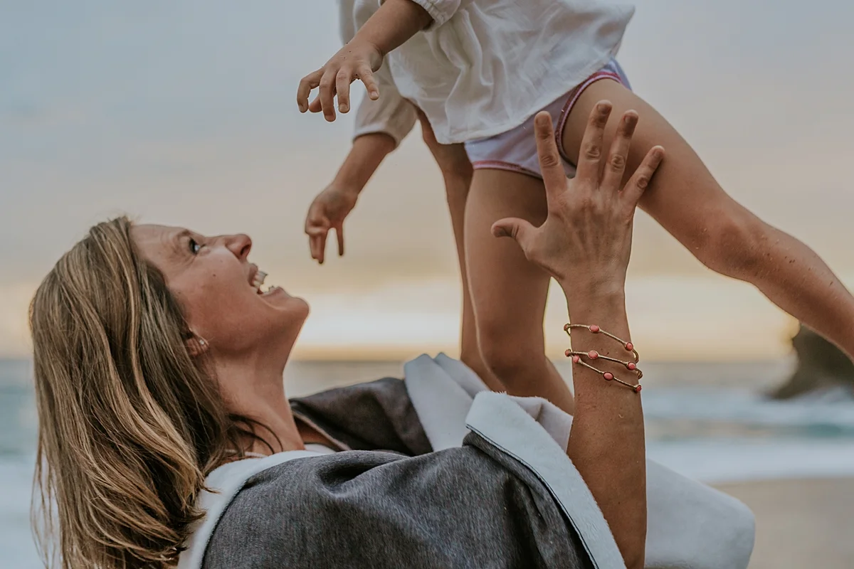 Orange County family photographer. Image of mom throwing her two year old daughter in the air during fun family photo beach session at Laguna Beach