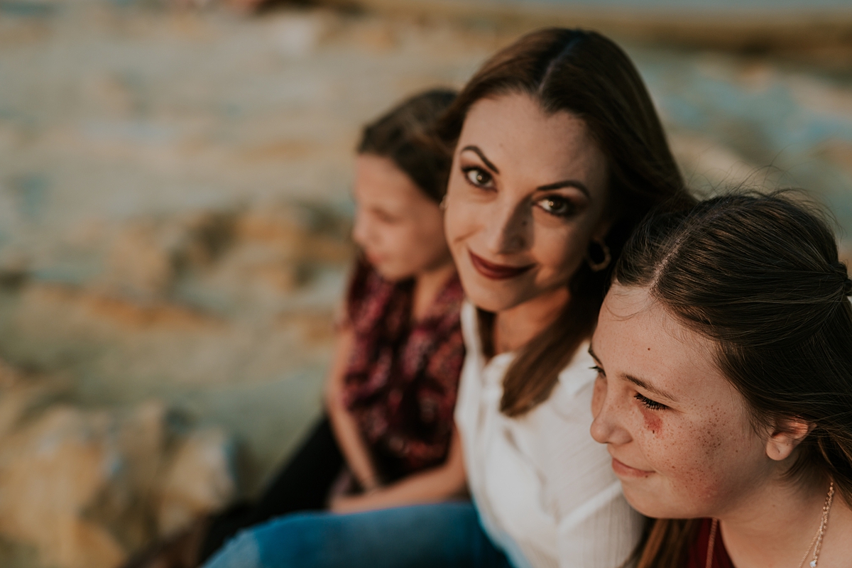 Orange County family photographer. Photo of mom and her daughters looking at the sunset as mom looks at the camera during family photo session at Top of the World Laguna Beach