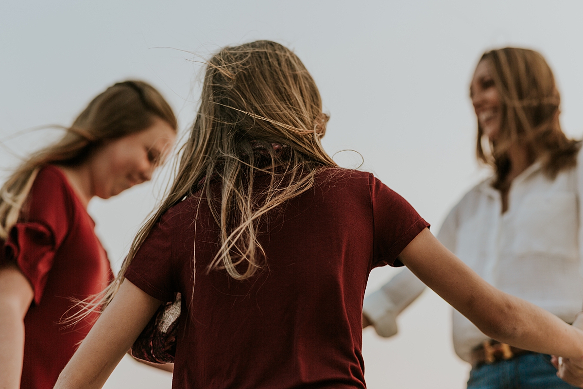 Orange County family photographer. Photo of mom and her daughters holding hands and skipping around laughing during candid family photo session at Top of the World Laguna Beach