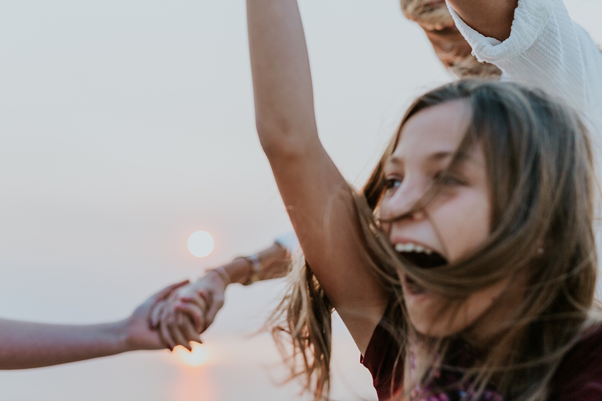 Orange County family photographer. Photo of mom and her daughters holding hands and skipping around laughing during candid family photo session at Top of the World Laguna Beach