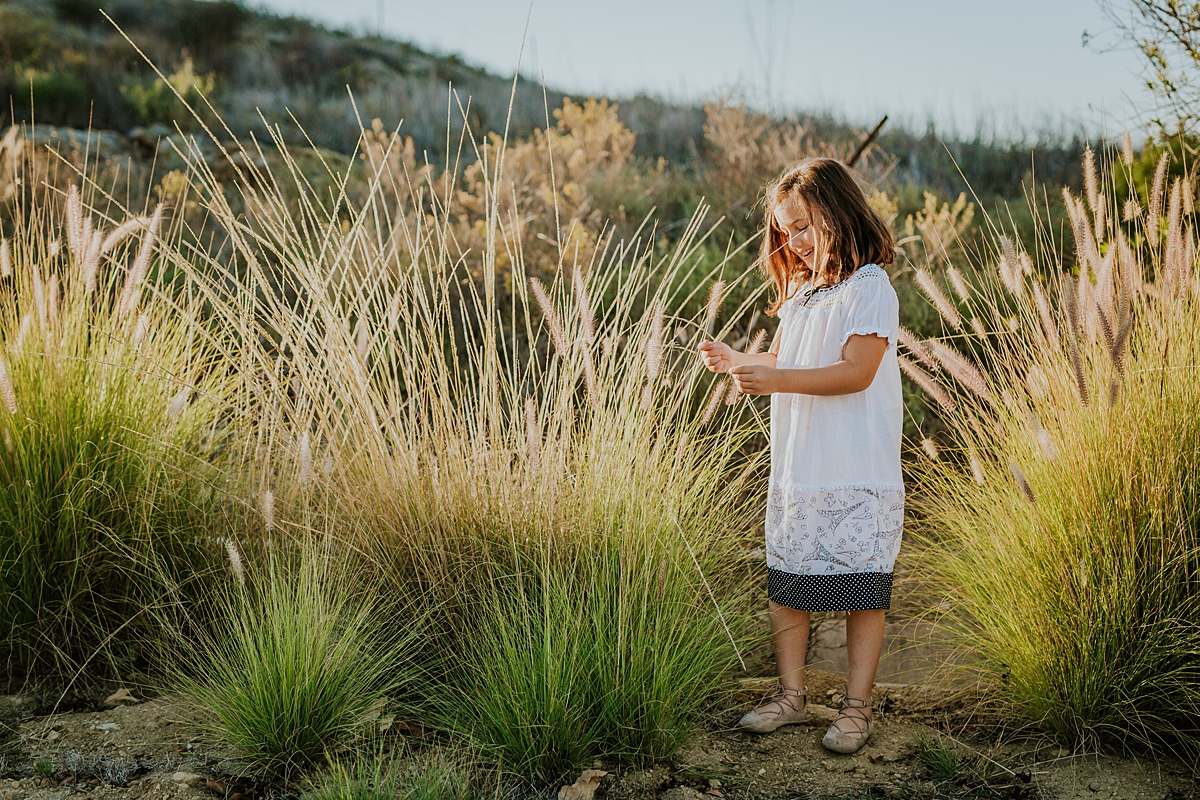 Orange County family photographer. Photo of beautiful 5 year old girl in white dress picking the dandelions at sunset at family photo shoot at Quail Hill