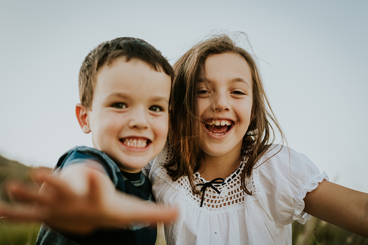 Orange County family photographer. Candid photo of brother and sister laughing and reaching for the camera at family photo shoot at Quail Hill