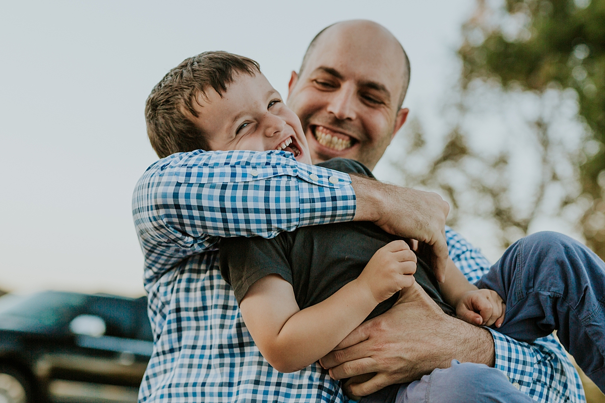 Orange County family photographer. Candid photo of dad tickling his youngest son during family photo shoot at Quail Hill with Krystil McDowall Photography