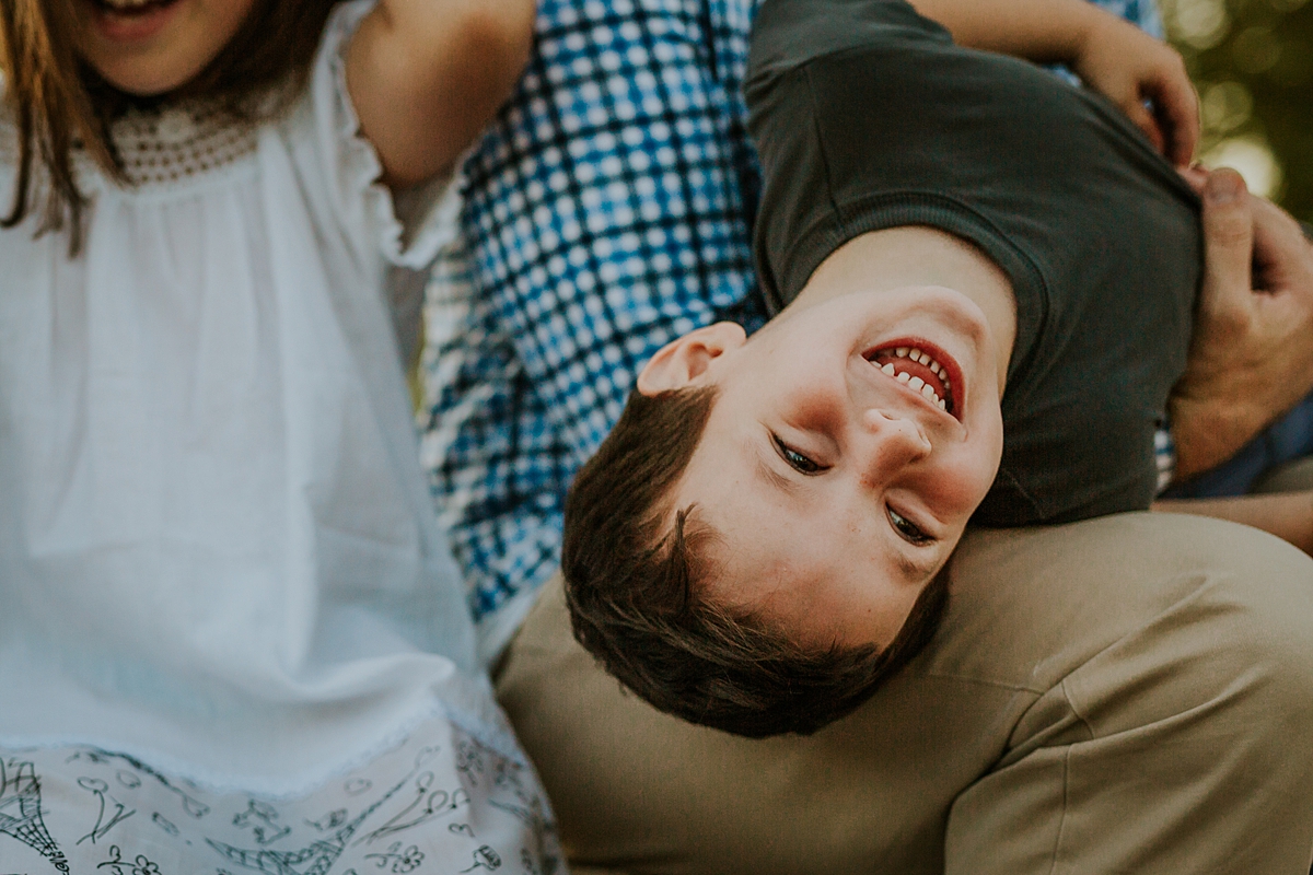 Orange County family photographer. Candid photo young boy strewn across his dad's lap laughing during family photo shoot at Quail Hill with Krystil McDowall Photography