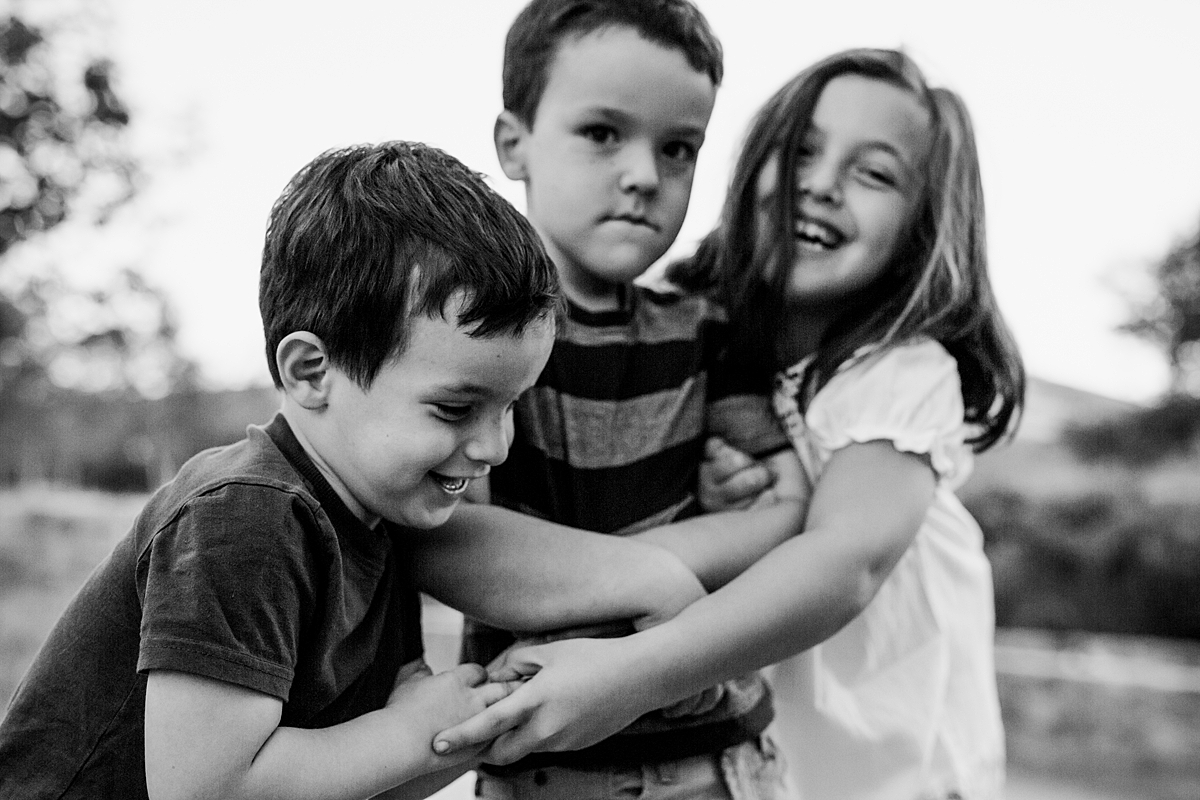 Orange County family photographer. Candid photo of three siblings laughing as they play games with each other during family photo shoot at Quail Hill with Krystil McDowall Photography