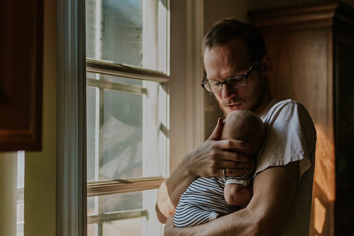Orange County family photographer. Photo of dad and his newborn son as they stand near light filled window during in home newborn session with Krystil McDowall Photography