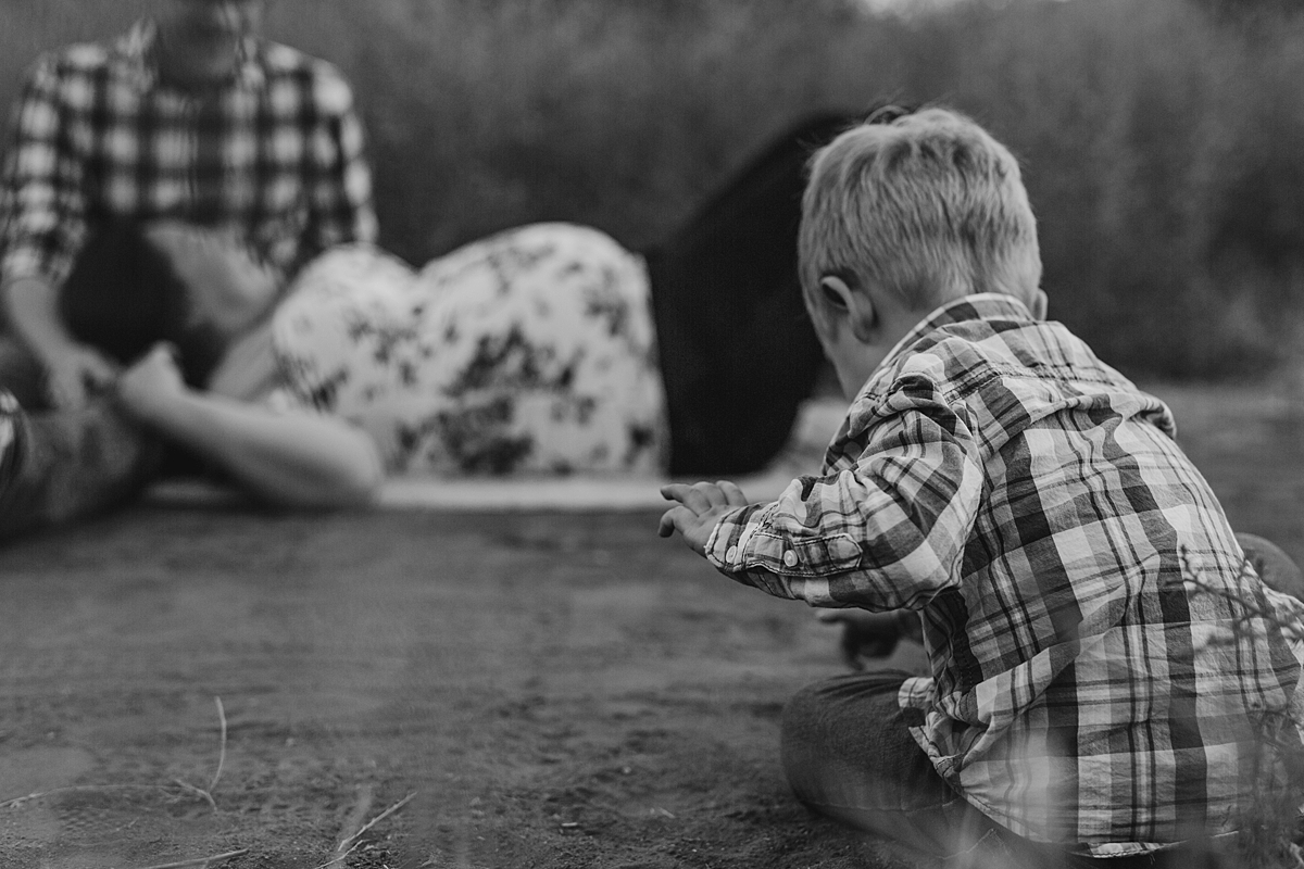 Orange County family photographer. Photo of young boy playing in the dirt with his mom and dad in the background during outdoor maternity photo session at Irvine Regional Park