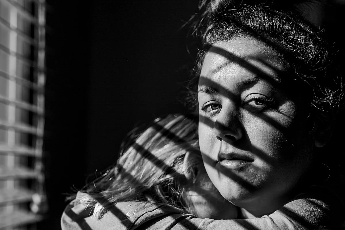 Orange County family photographer. Photo of mom holding her daughter while standing in sun drenched window in daughter's bedroom during in home family photo session in Long Beach