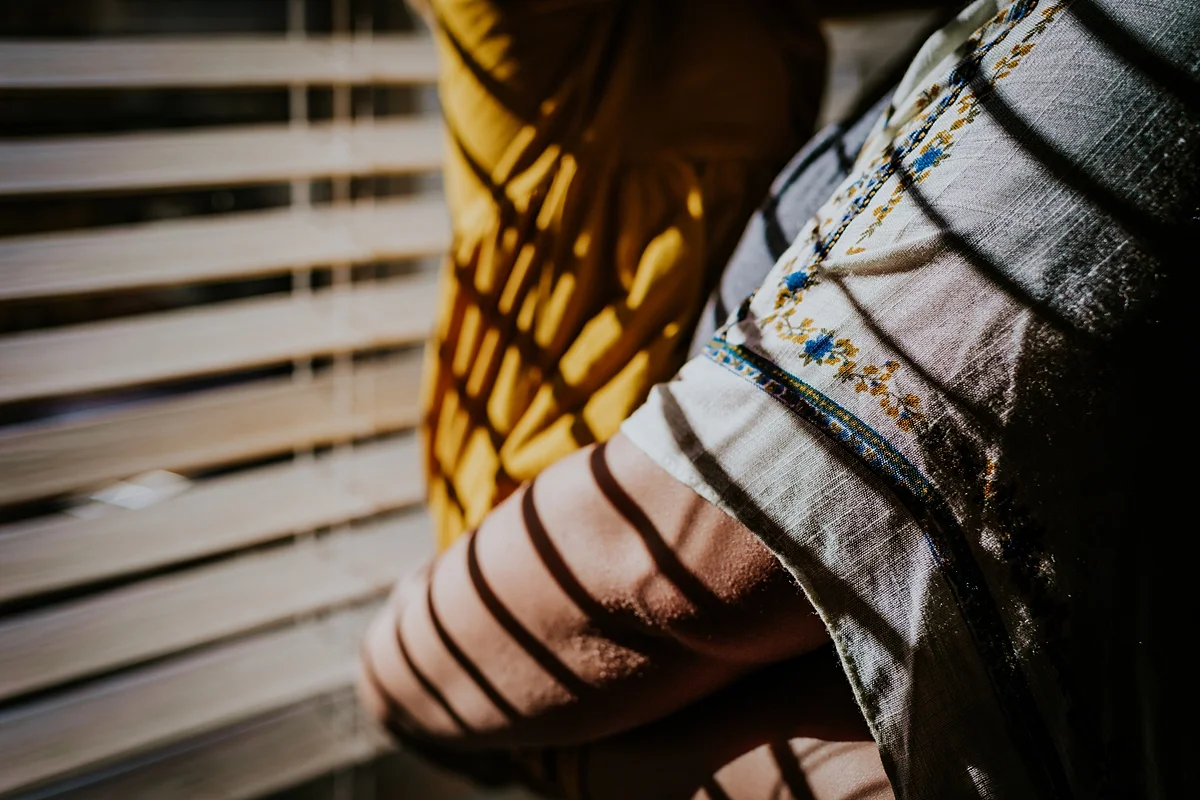 Orange County family photographer. Details photo of mom's arms wrapped around her daughter while standing in sun drenched window in daughter's bedroom during in home family photo session in Long Beach
