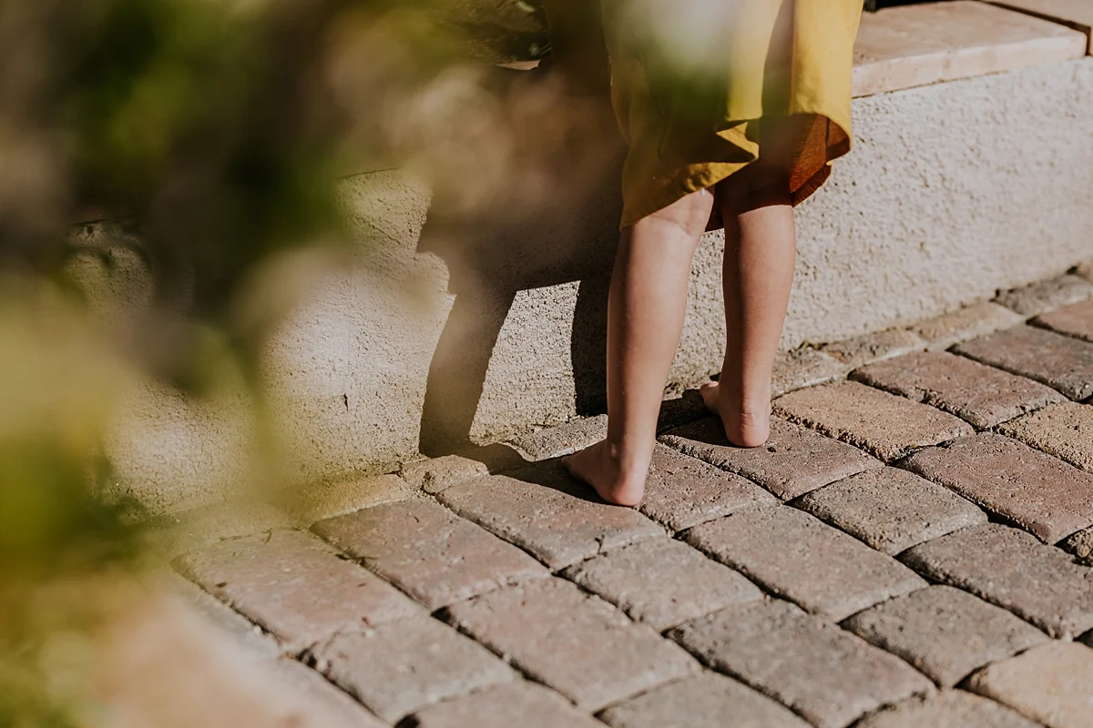 Orange County family photographer. Details photo of daughter in her mustard dressing picking flowers from the garden during in home family photo session in Long Beach, CA