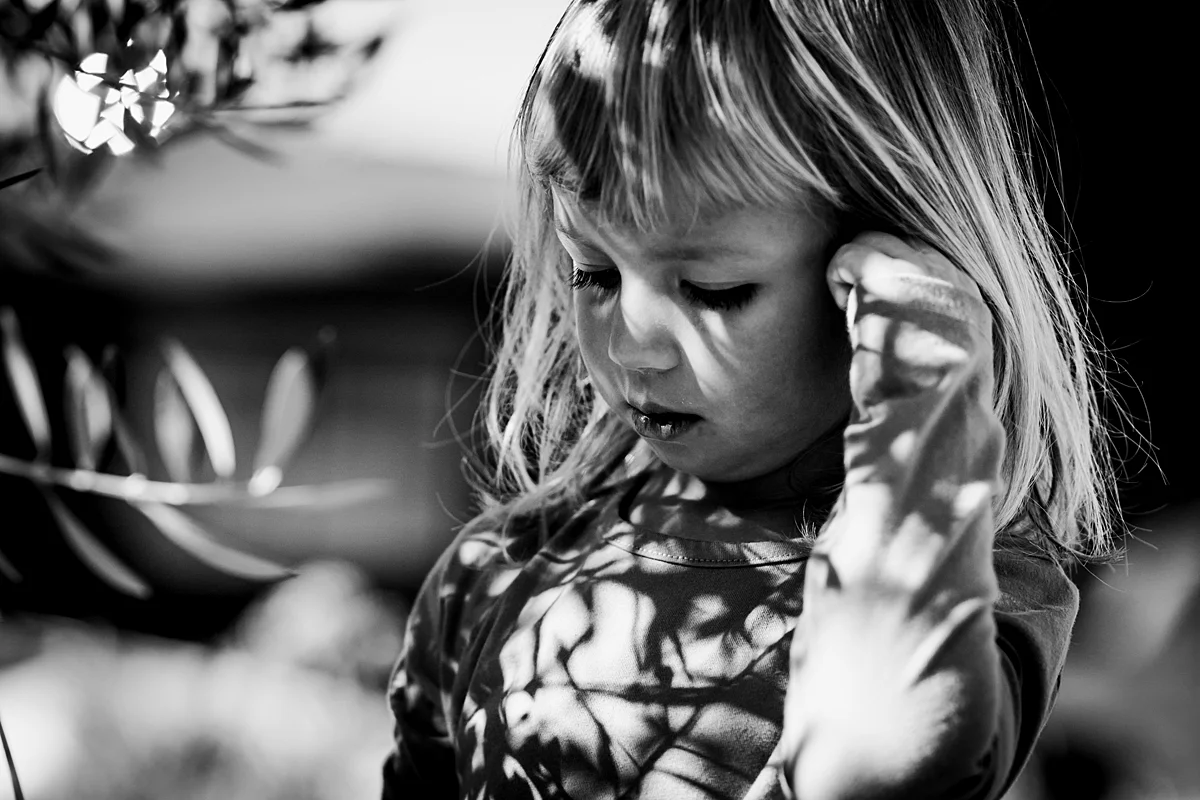 Orange County family photographer. Photo of girl in her front yard in the shadows of the bush out front during in home family photo session in Long Beach, CA