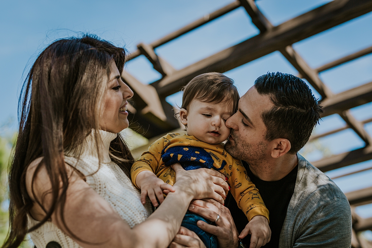 Orange County family photographer. Candid photo of mom, dad and one year old boy taken from below on blue sky day during family photo session in Irvine CA