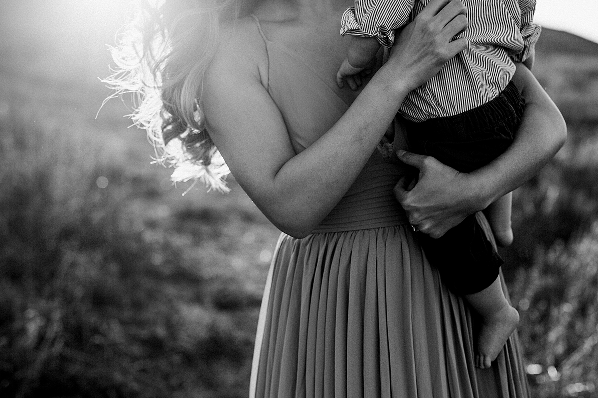 Orange County family photographer. Backlit image of mom holding her sweet ten month old boy during outdoor family photo session at Quail Hill Trailhead Irvine