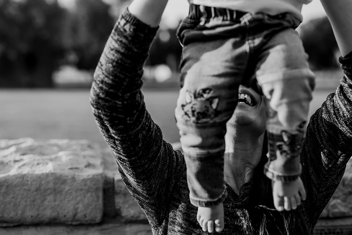 Orange County family photographer. Black and white photo of mom holding her sweet one year old in the air at Jeffrey Open Space Train Irvine