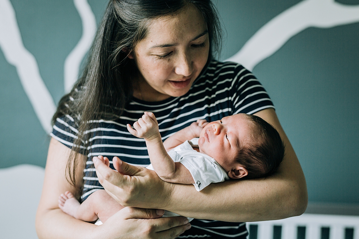 Orange County family photographer. Photo of mom holding her sweet newborn son in the baby’s nursery during newborn photo shoot in Lake Forrest Orange County