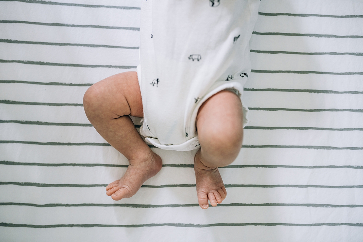 Orange County family photographer. photo of newborn baby feet as he lays on striped sheets in his crib during newborn photo shoot in Lake Forrest Orange County