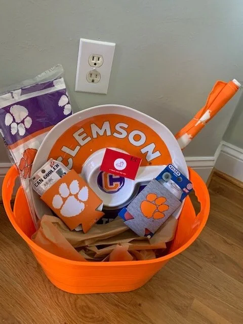 “CLEMSON ALL THE WAY” BASKET You’ll look as prepared as our team is with your car swag, table cloth, koozies and platter. Not to mention you’ll be ready to host the next amazing tailgate with this $50 gift card to Chick-fil-A to get your chicken minis or nuggets. DONOR: 2nd Grade Classes VALUE: $115