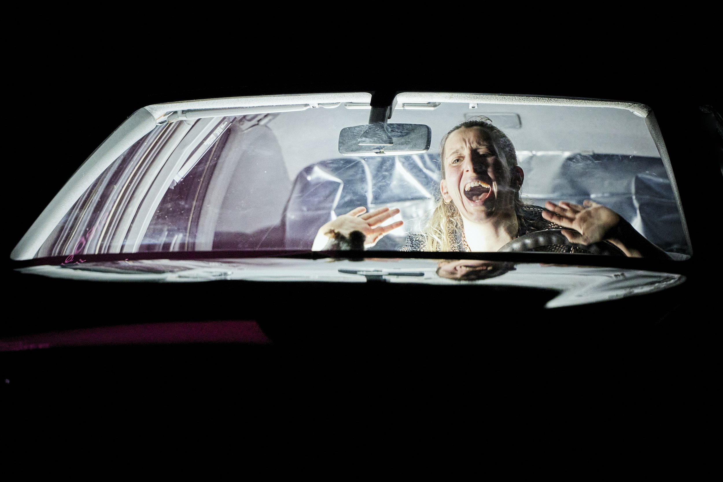  A close up of a person in a lit car with their hands up shouting. 