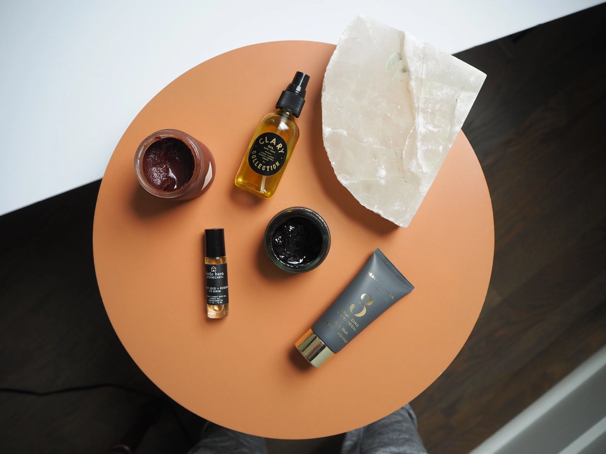 Assorted skincare and beauty products on a round orange table with a stone slab.