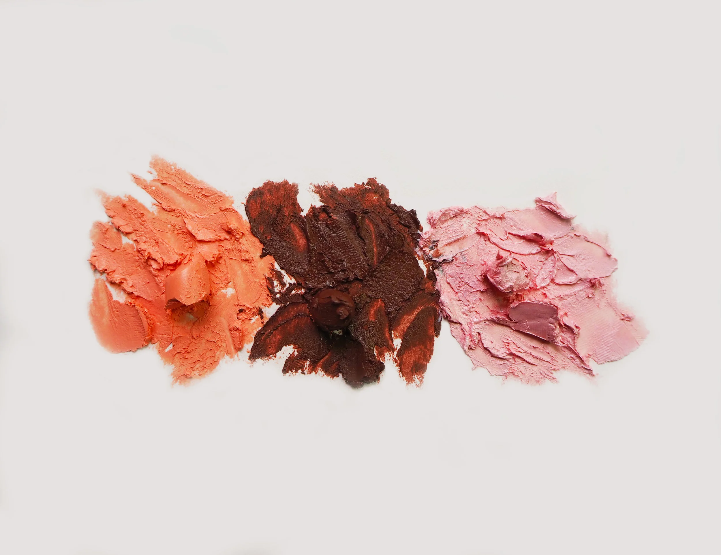 Three smears of makeup in orange, brown, and pink on a white background.
