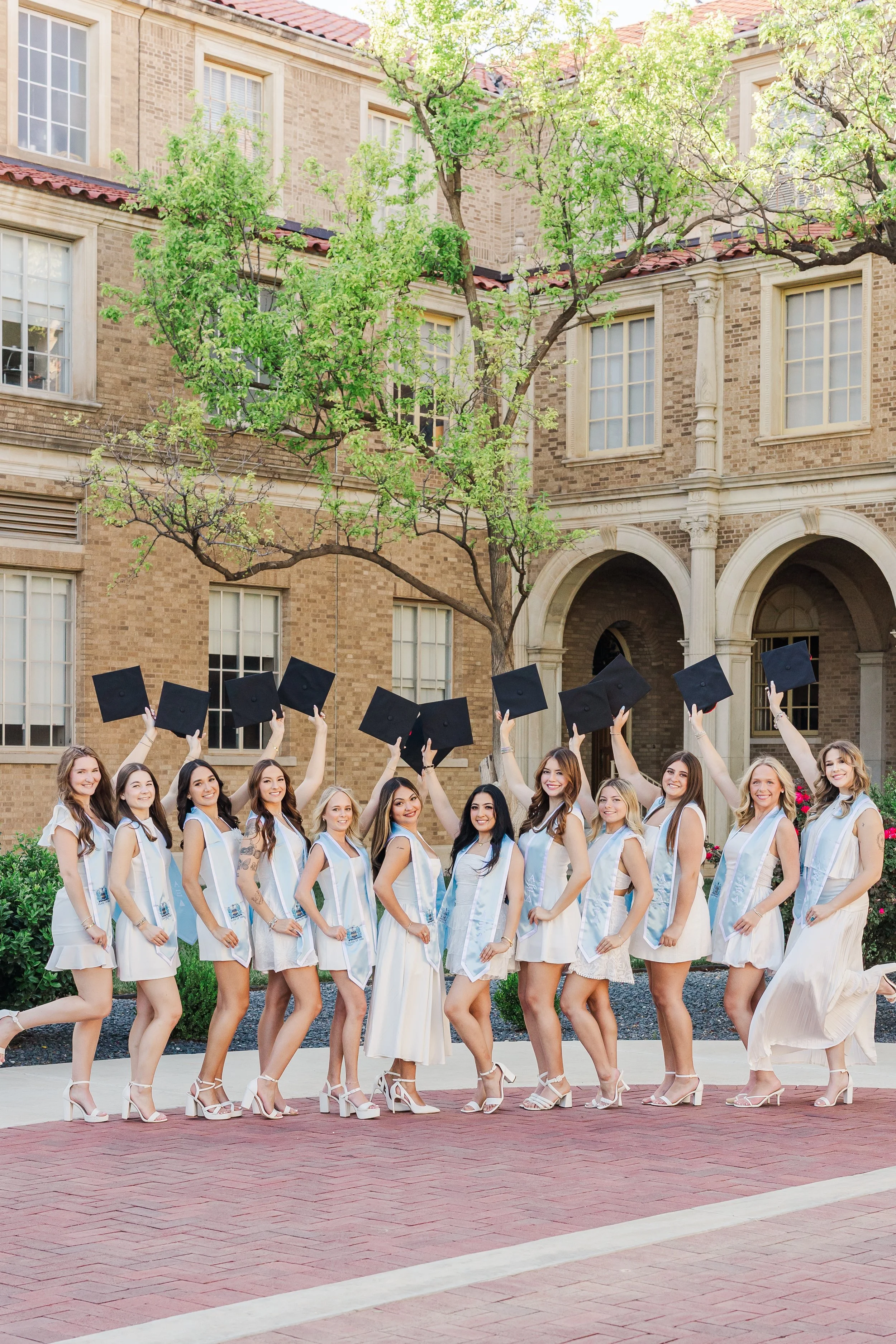 texas tech sorority friend group posing while holding their sorority stole and throwing their graduation cap behind them.