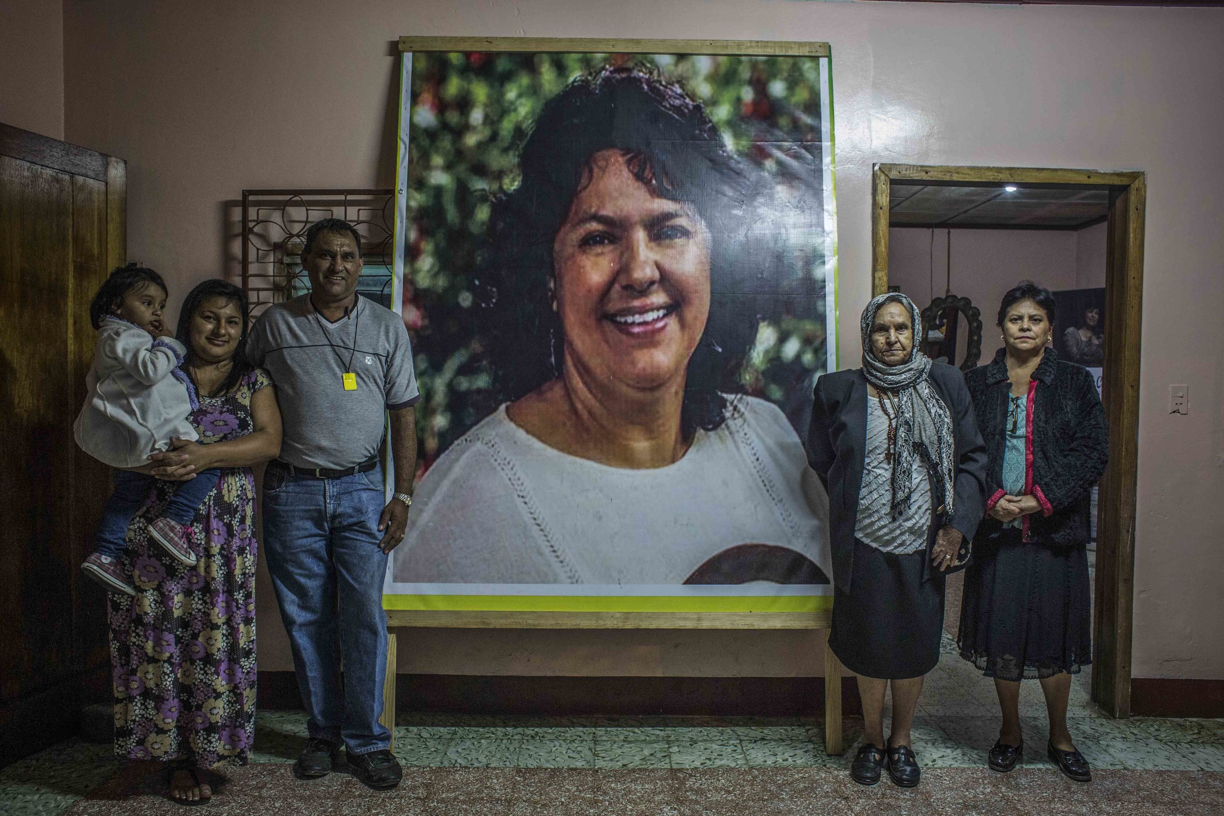 The family of Berta Caceres, mother's sister and brother-in-law with her daughter, posing next to poster of Berta , affixed at the entrance of the family home, in the city of La Esperanza, Honduras.
