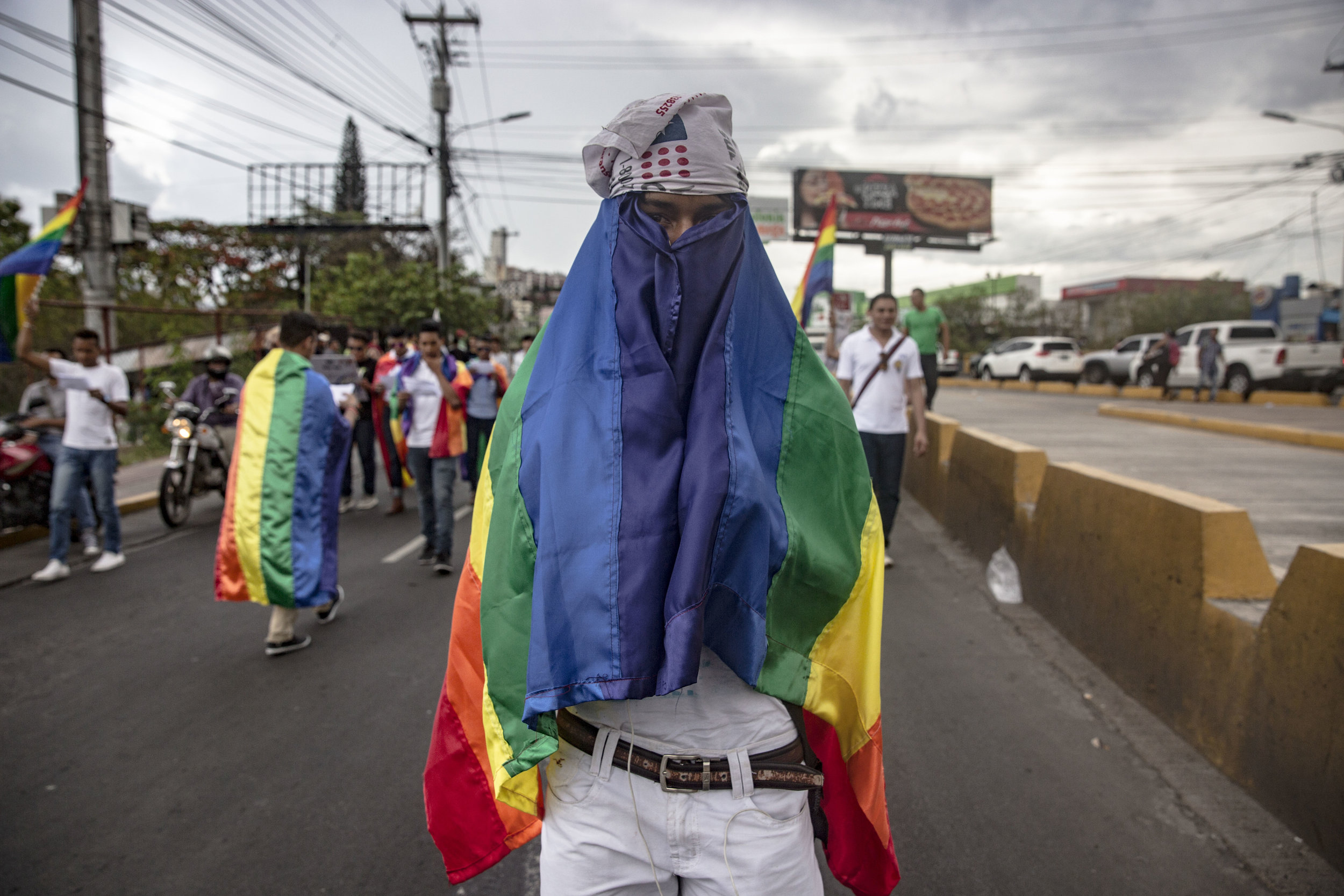  A guy hides his   face while taking part at the Gay Pride parade in May 2016, Tegucigalpa, Honduras. Homosexuality in Honduras is not a crime itself, however, LGBT community members are afraid to be identified and target while out of the crowd.  
