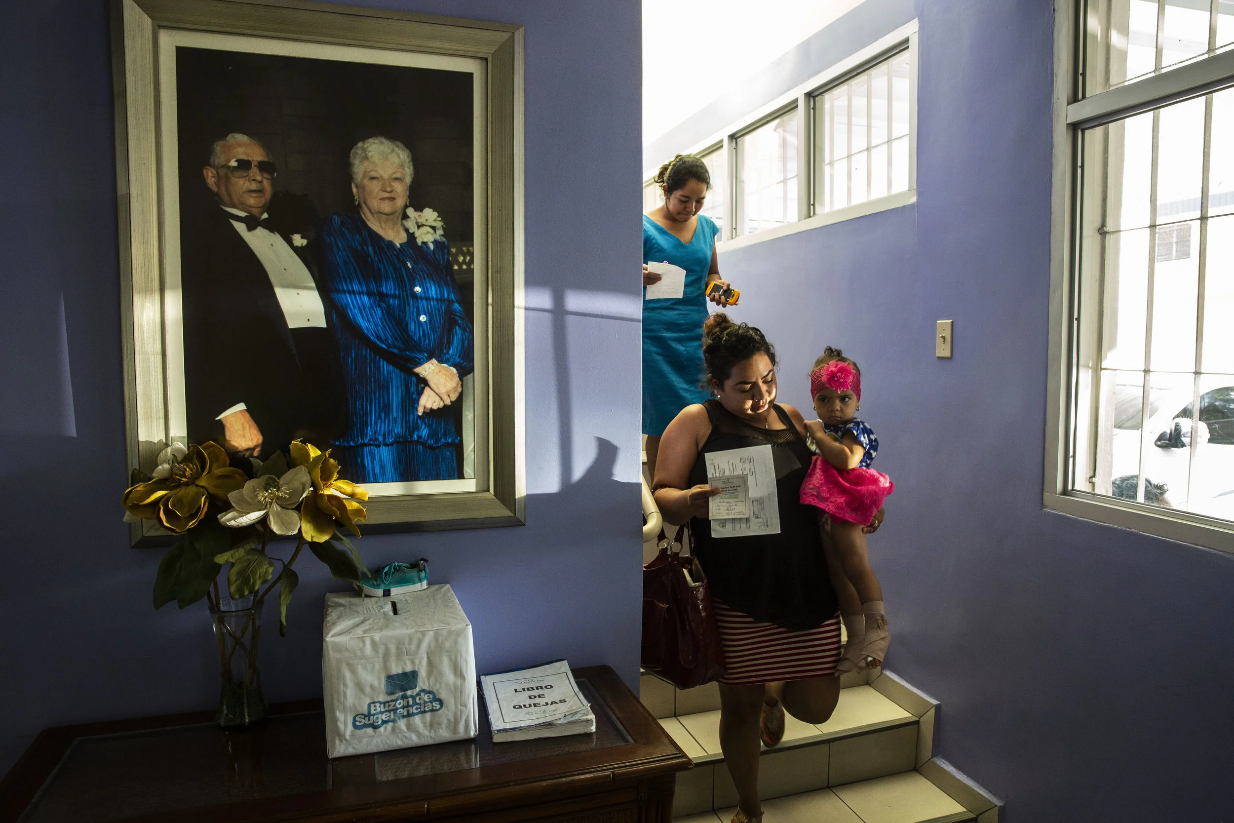 Inside the Ruth Paz hospital in San Pedro Sula, mothers of patients walk near the portrait of Madam Ruth Paz and her honduran husband Josè, who started the fundatation.