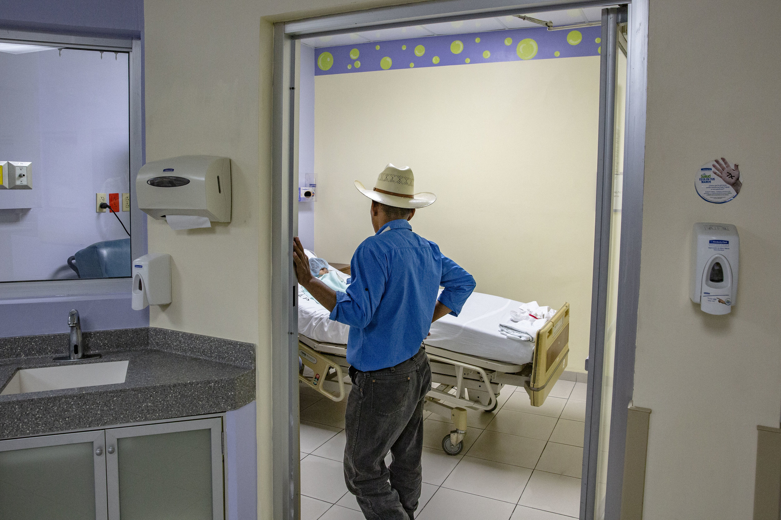 Late at night a father watches her little duaghter who was operated at the heart during the day by a brigade of foreign surgeons at the Ruth Paz hospital in San Pedro Sula, Honduras.