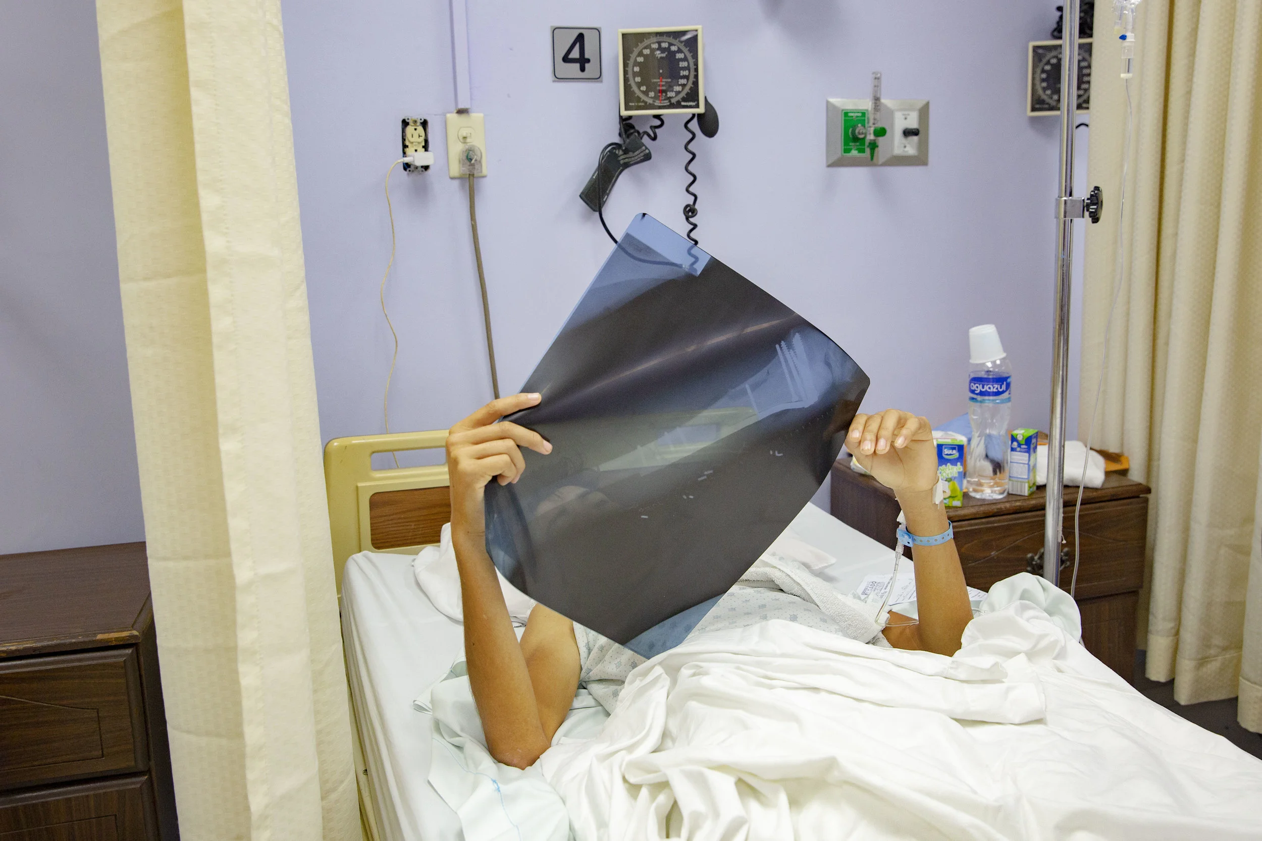 Franklin Lopez, 19, lies in a bed looking at the results of an ultrasound exam at the Ruth Paz hospital in San Pedro Sula, Honduras. He broke his femur when he was on a motorbike with his friend. “We were just playing, it was an accident” he says, visibly in pain. After the accident he spent twenty-one days at the public hospital without being treated for his fracture, then his mother took him to the Ruth Paz hospital an he was operated three days after his arrival.