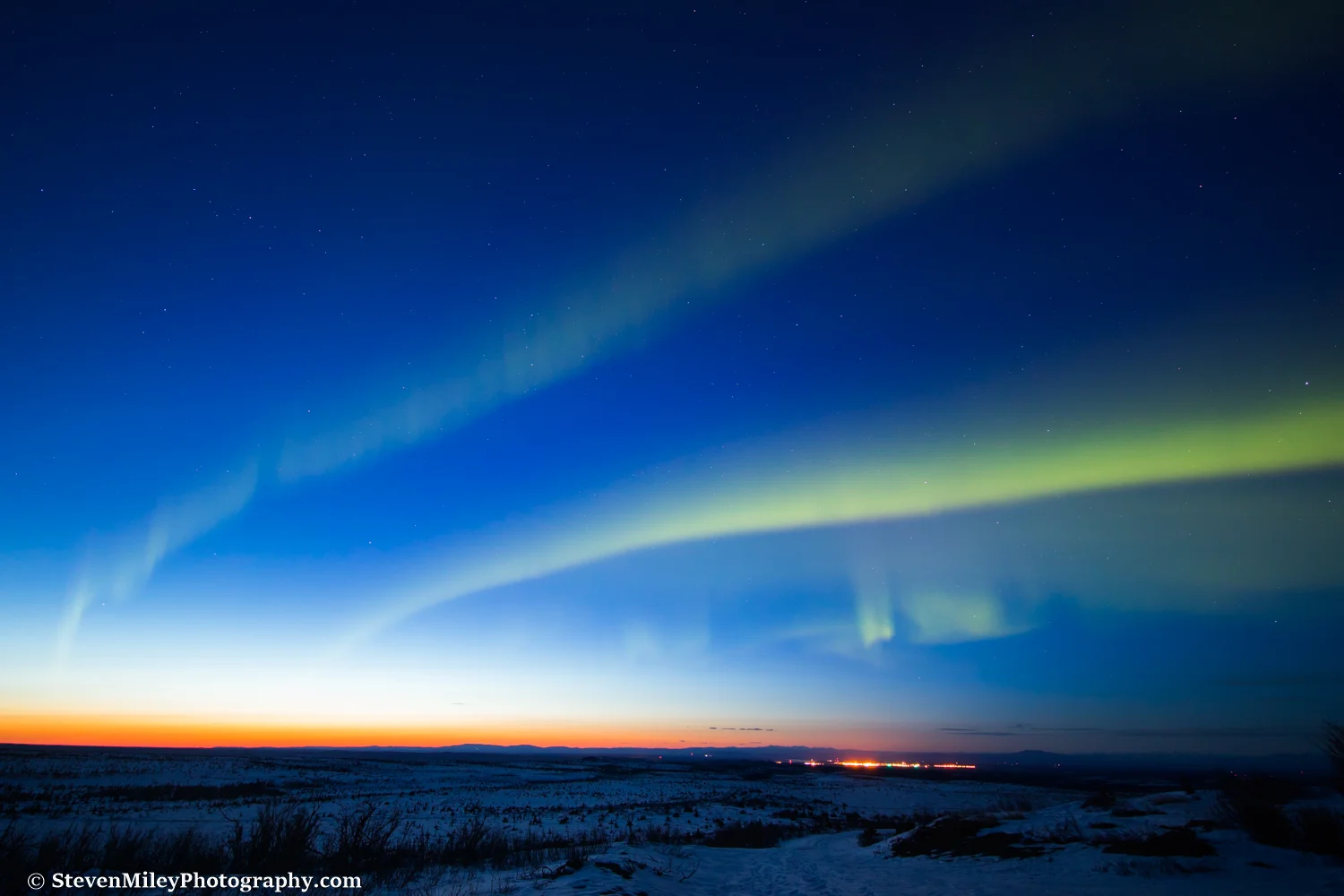 Aurora borealis dancing during twilight above the lights of Fort Greely.