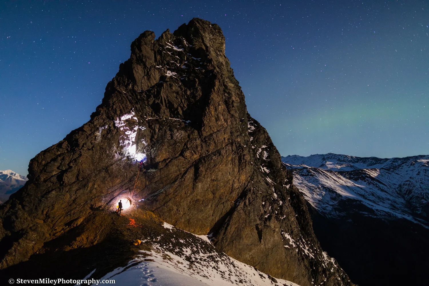 Grant climbing Devils Thumb in the dark with Matt belaying. The rising moon is casting a warm glow on the mountains.