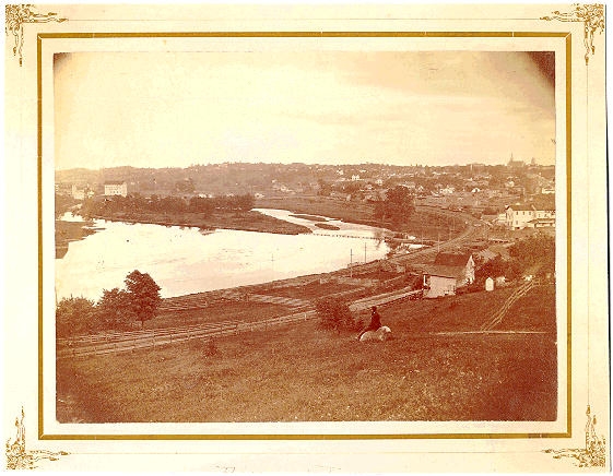 1870s photograph of riverfront, railroad, and mills in distance