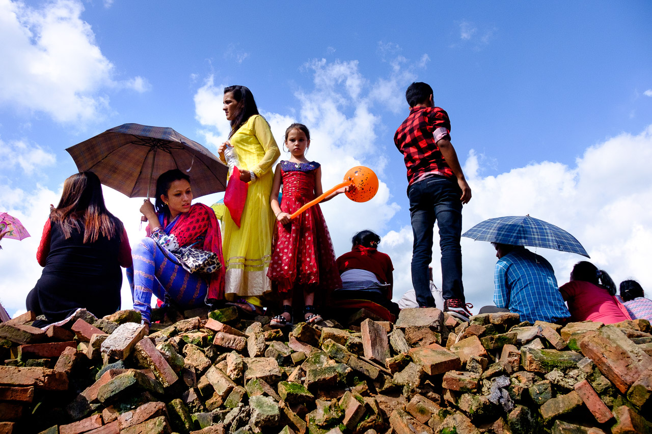   Gai Jatra Festival in Bhaktapur. Spectators stand on a pile of bricks in the main square to view the procession of beautiful decorated chariots that parade through the town to celebrate the lives of deceased family members from the past year. Each chariot holds a photo of the dead person hung at it’s centre and is carried by the rest of the family. &nbsp;  