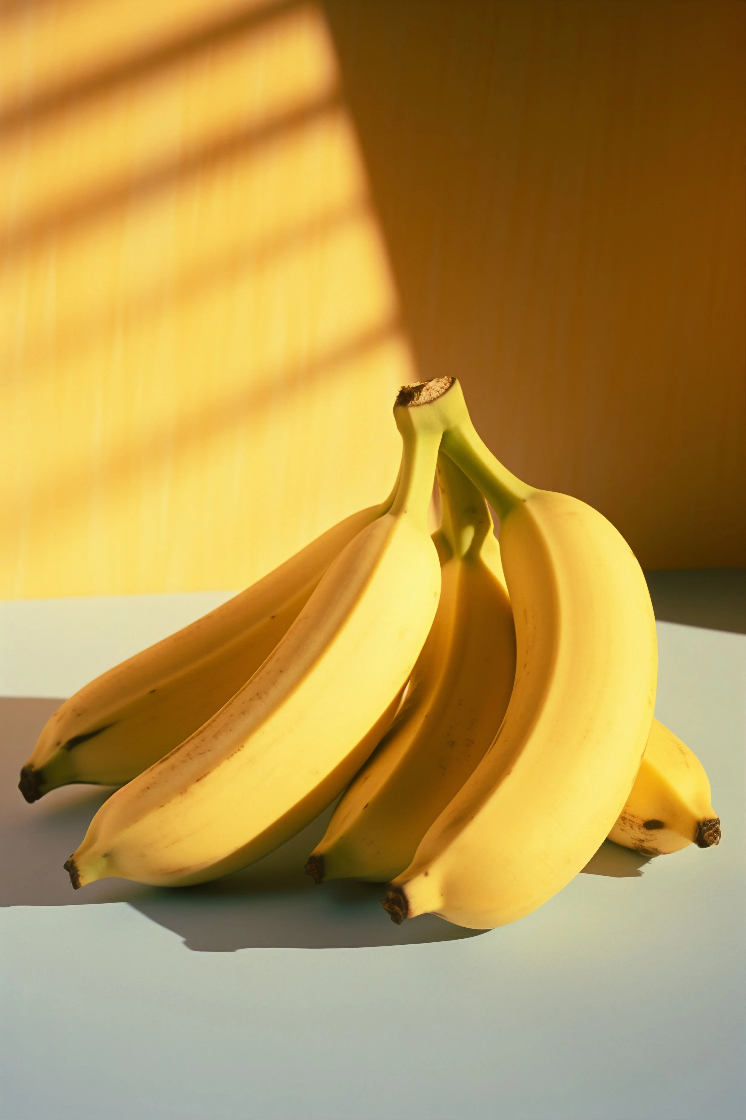 Cluster of ripe yellow bananas on a white surface with shadows cast by sunlight.
