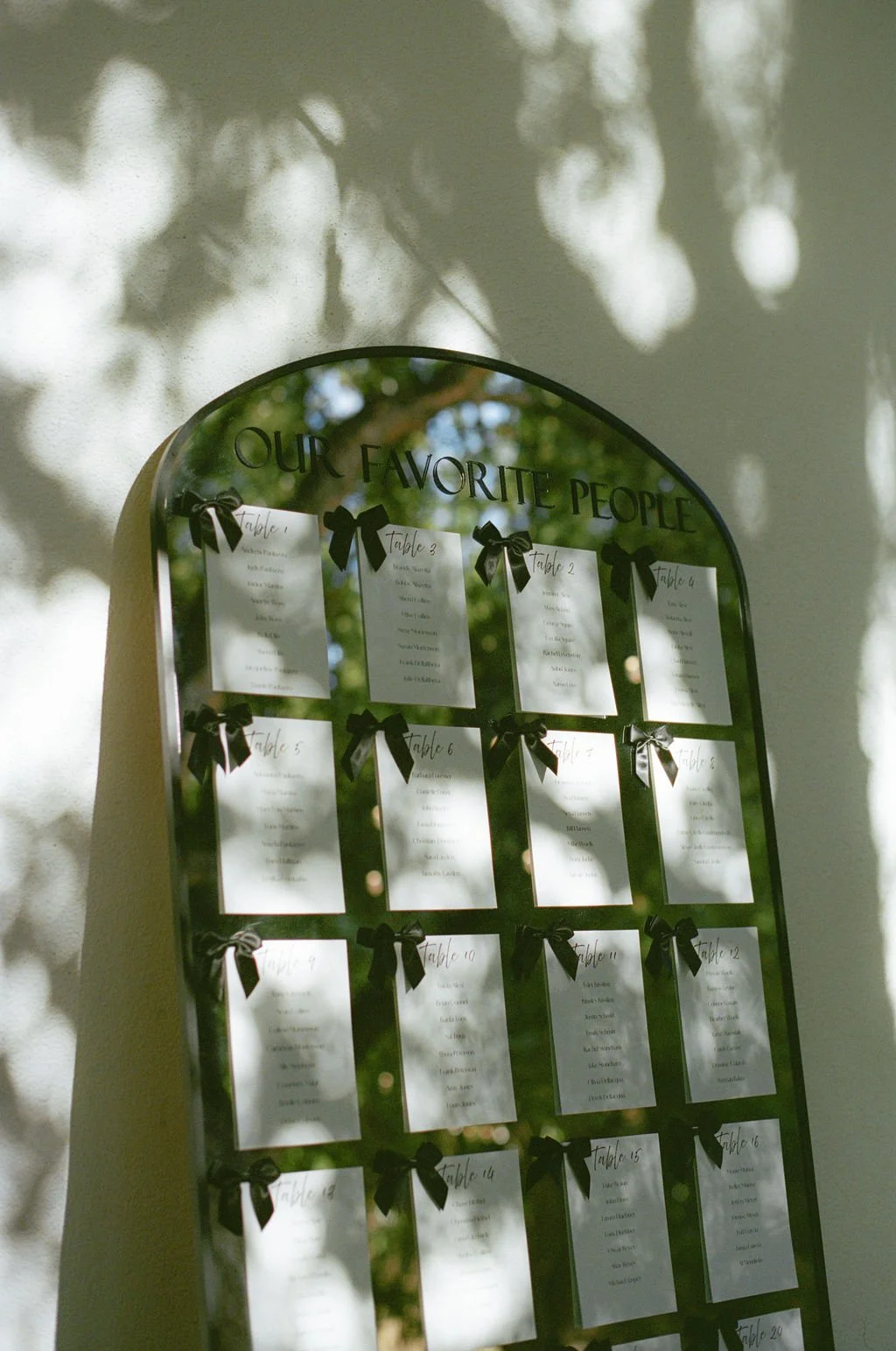 Mirror with a seating chart titled "Our Favorite People" reflecting trees and sunlight.