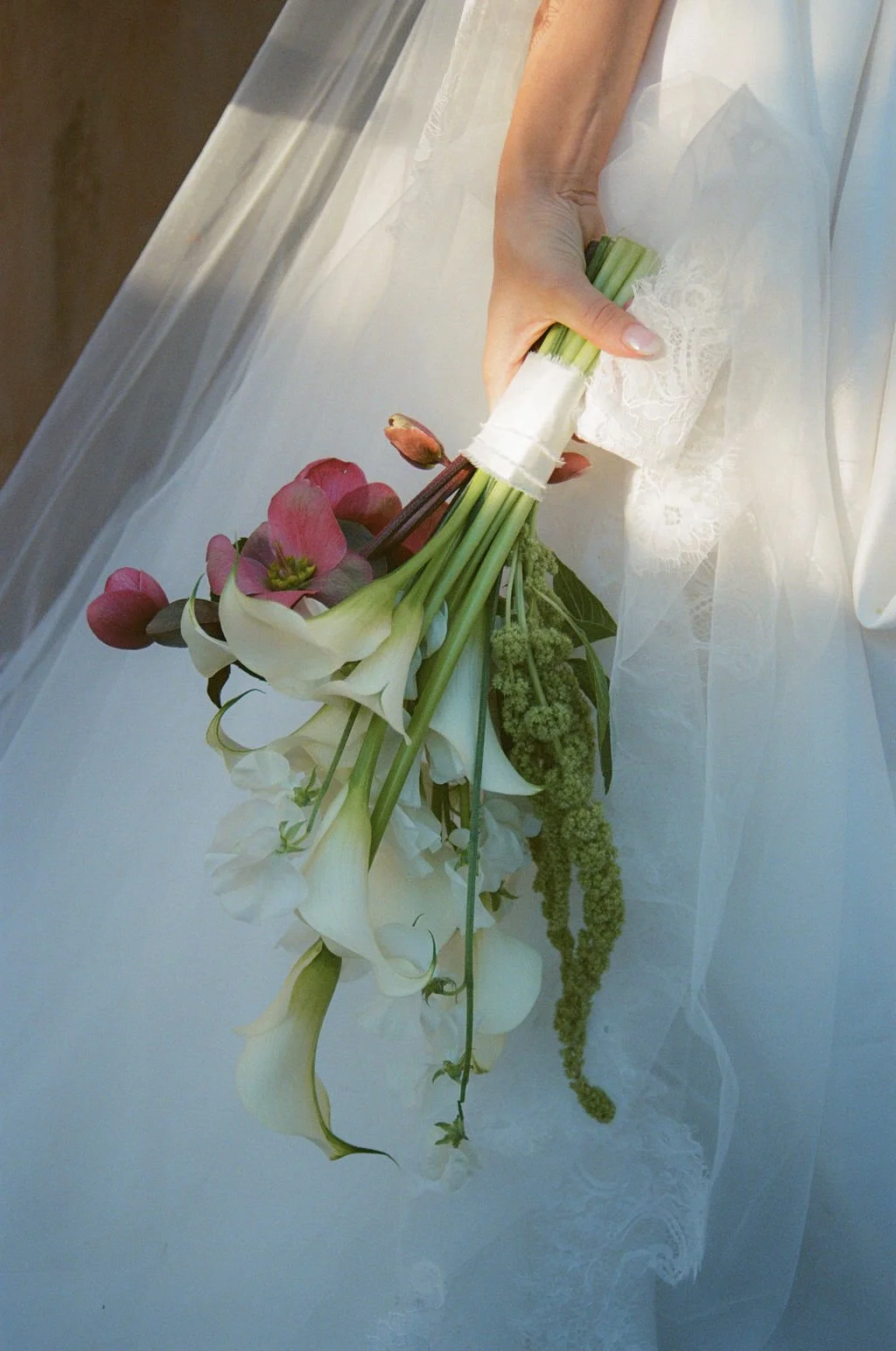 A woman in a white dress holding a bouquet of flowers with white lilies, pink bud flowers, and green foliage.