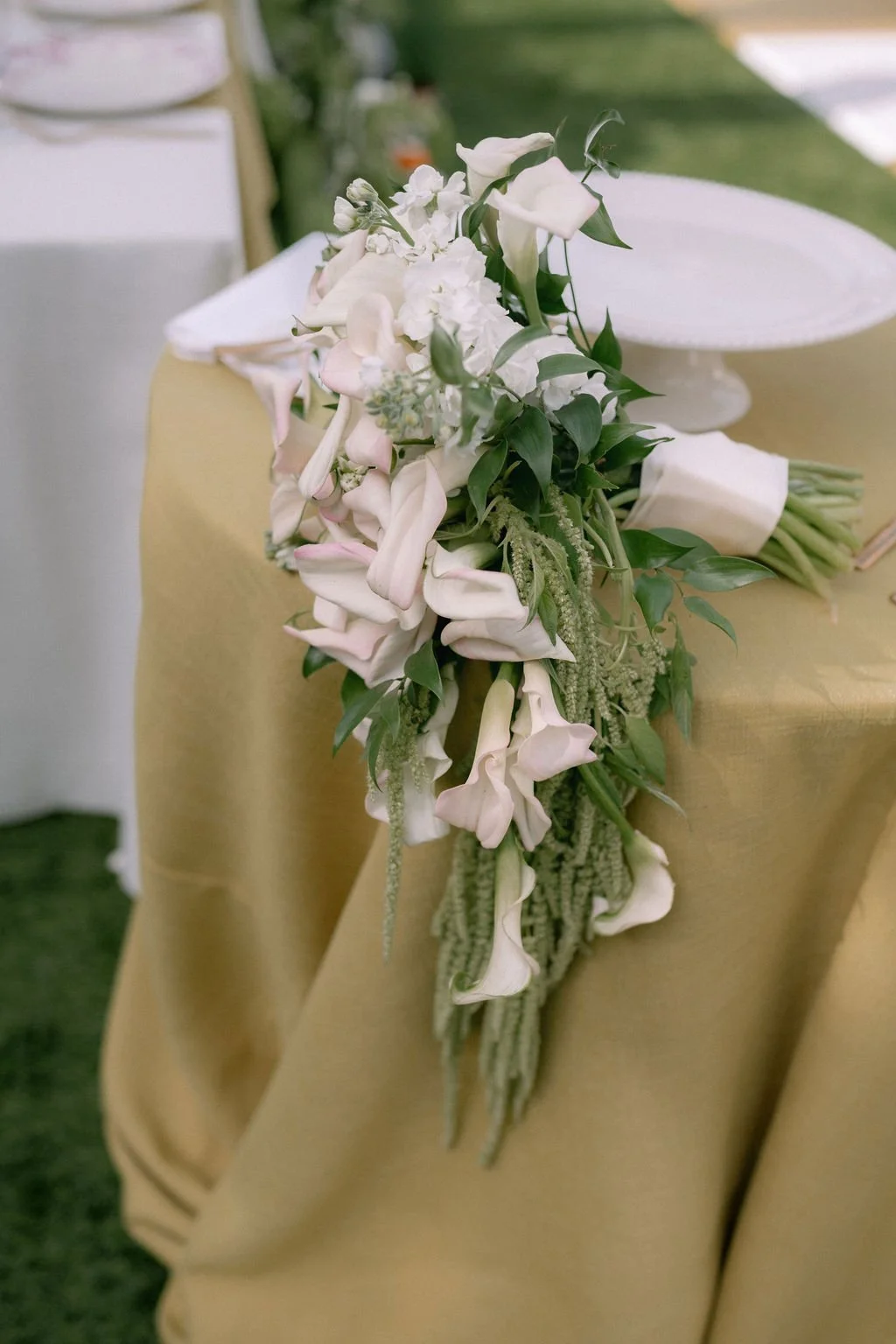 A cascading bouquet of white flowers and green leaves on a yellow tablecloth at a formal event.