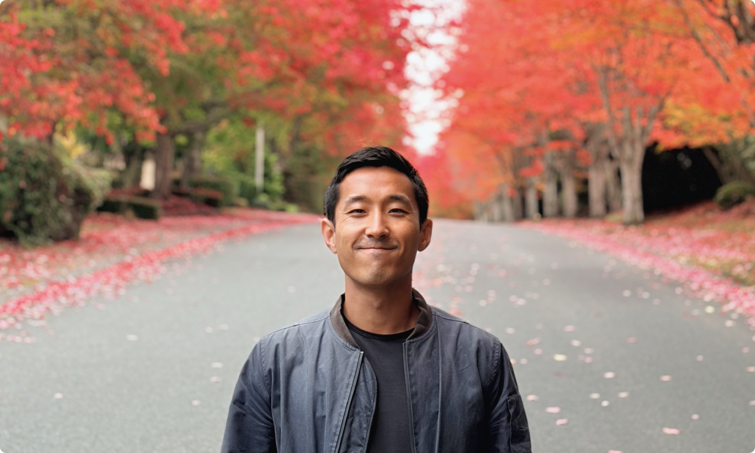 Zane Liu smiling and standing in front of a lush autumn foliage of red trees.
