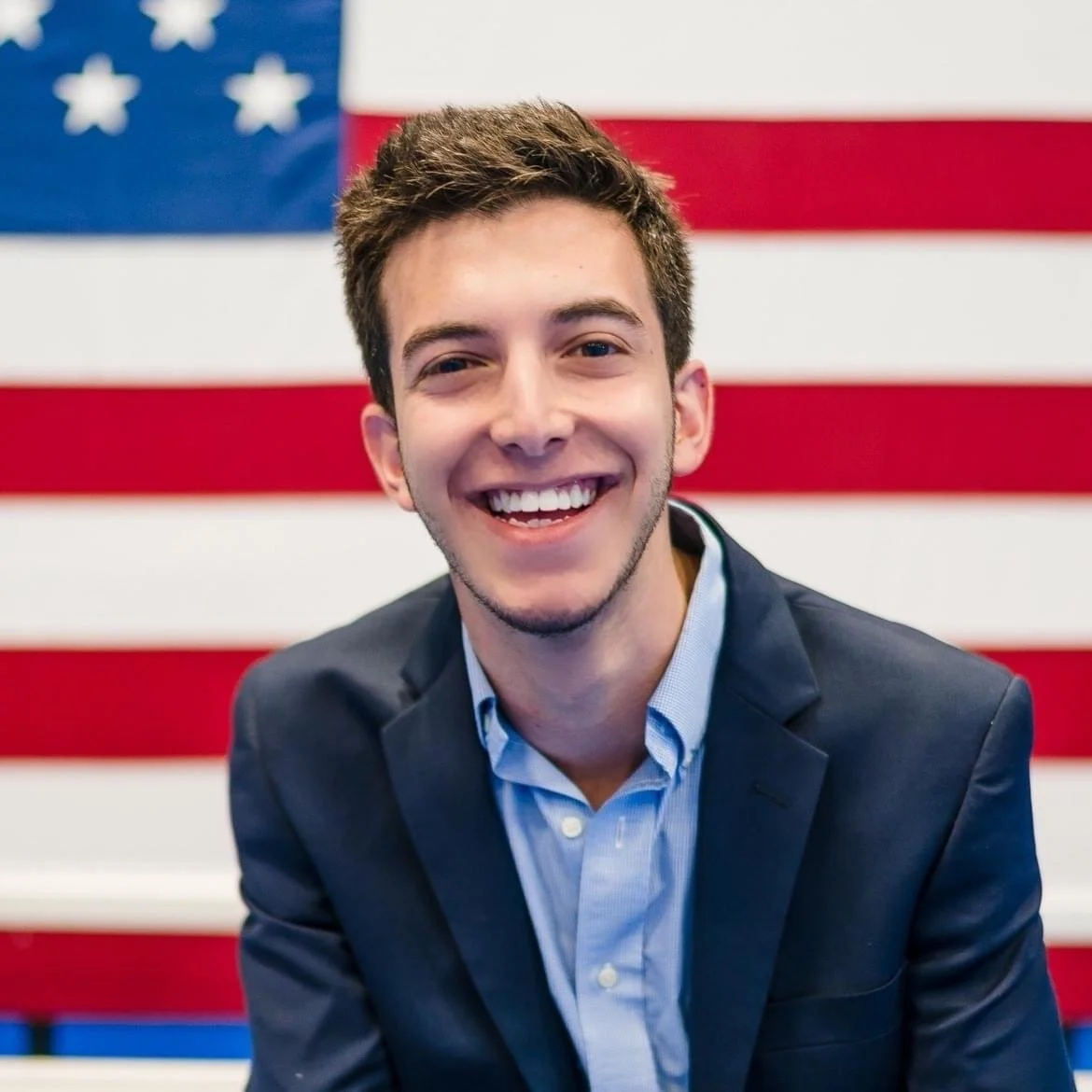 Young man smiling in front of an American flag.