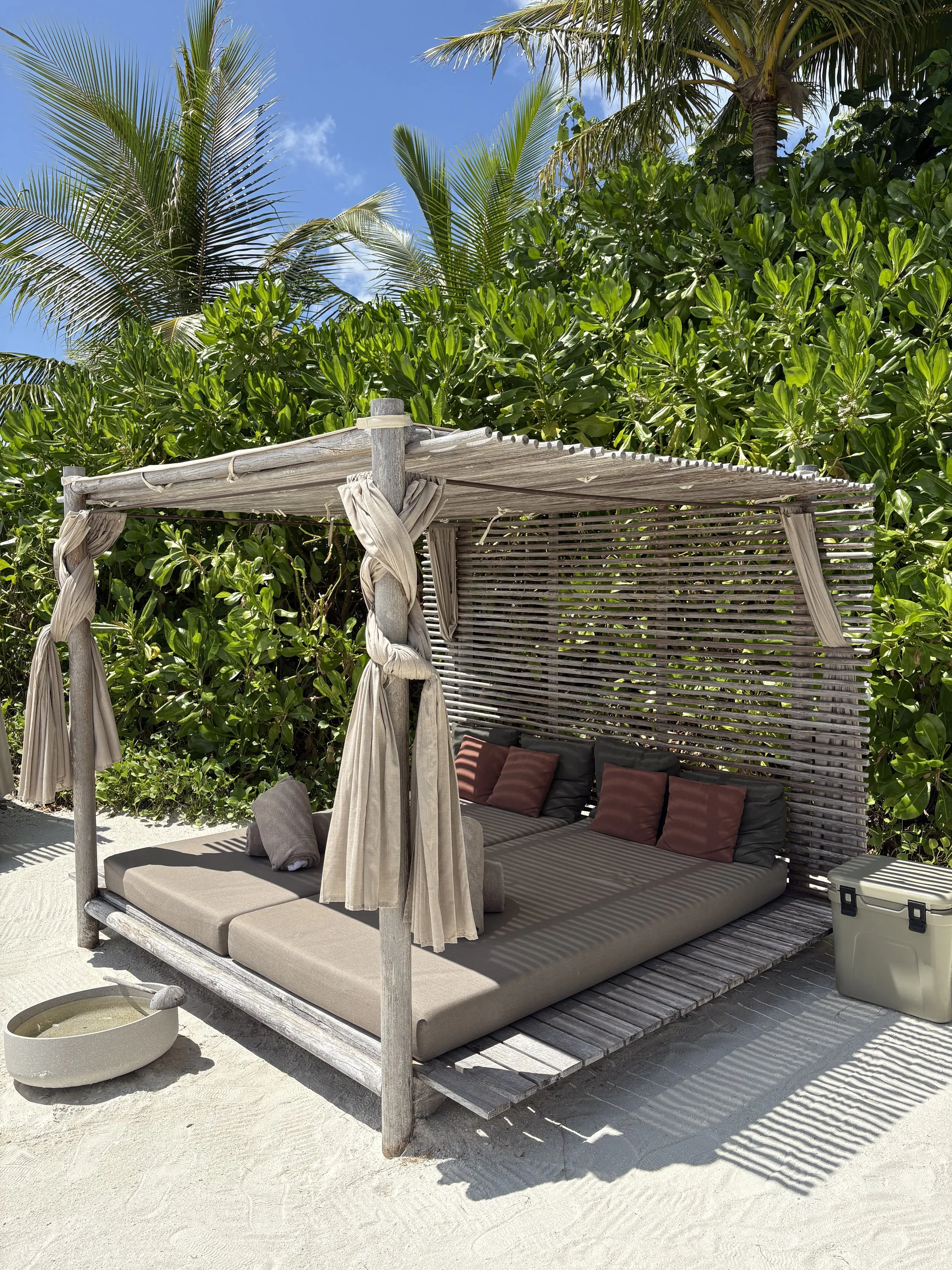 Cabana on the beach with cushions, towels, cooler and bowl to wash feet