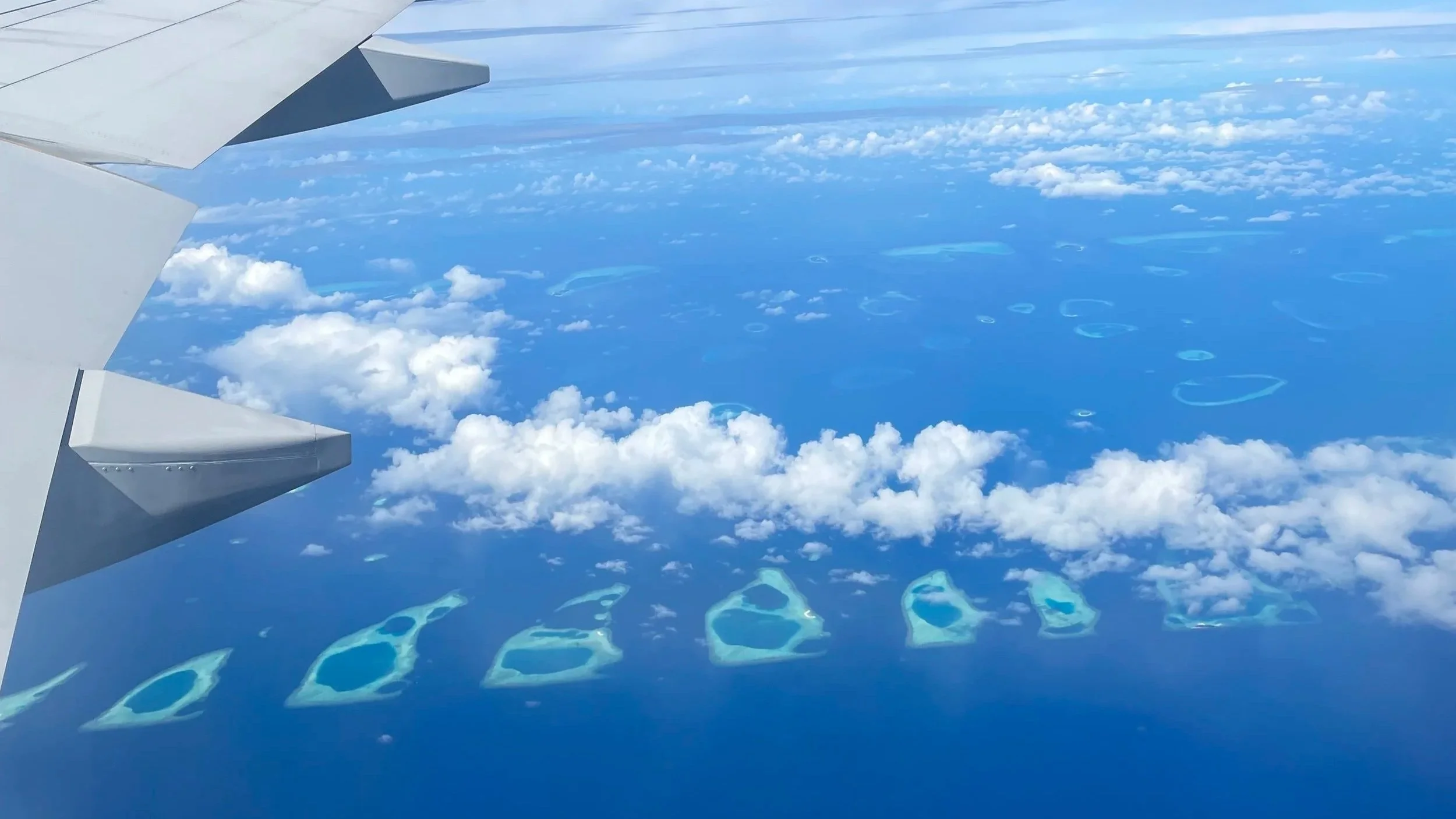 View from a plane window of clouds and Maldives Atoll formations