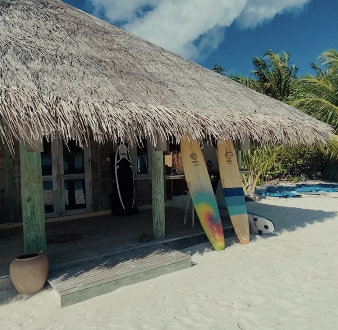 Thatched roof beach shack with two wooden surf boards leaning at the front